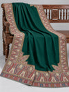 Close view of the emerald green Kani shawl's paisley border and corner motifs on a bench — Taj Mehal Handicrafts