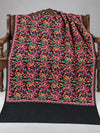 Black shawl with orange and green parrots, pink vines and colourful floral embroidery, displayed on a wooden bench with a plain edge | Taj Mehal Handicrafts