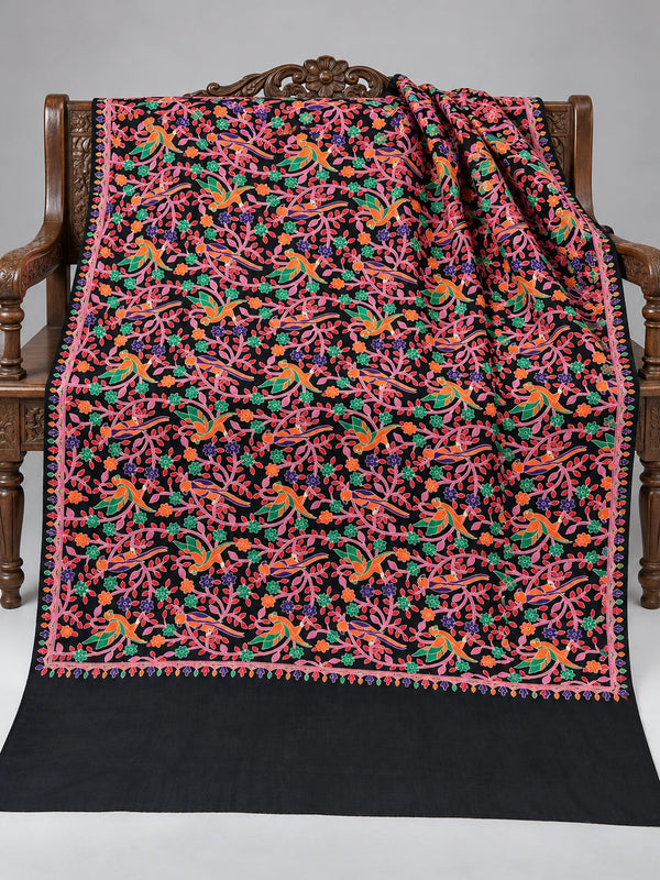 Black shawl with orange and green parrots, pink vines and colourful floral embroidery, displayed on a wooden bench with a plain edge | Taj Mehal Handicrafts